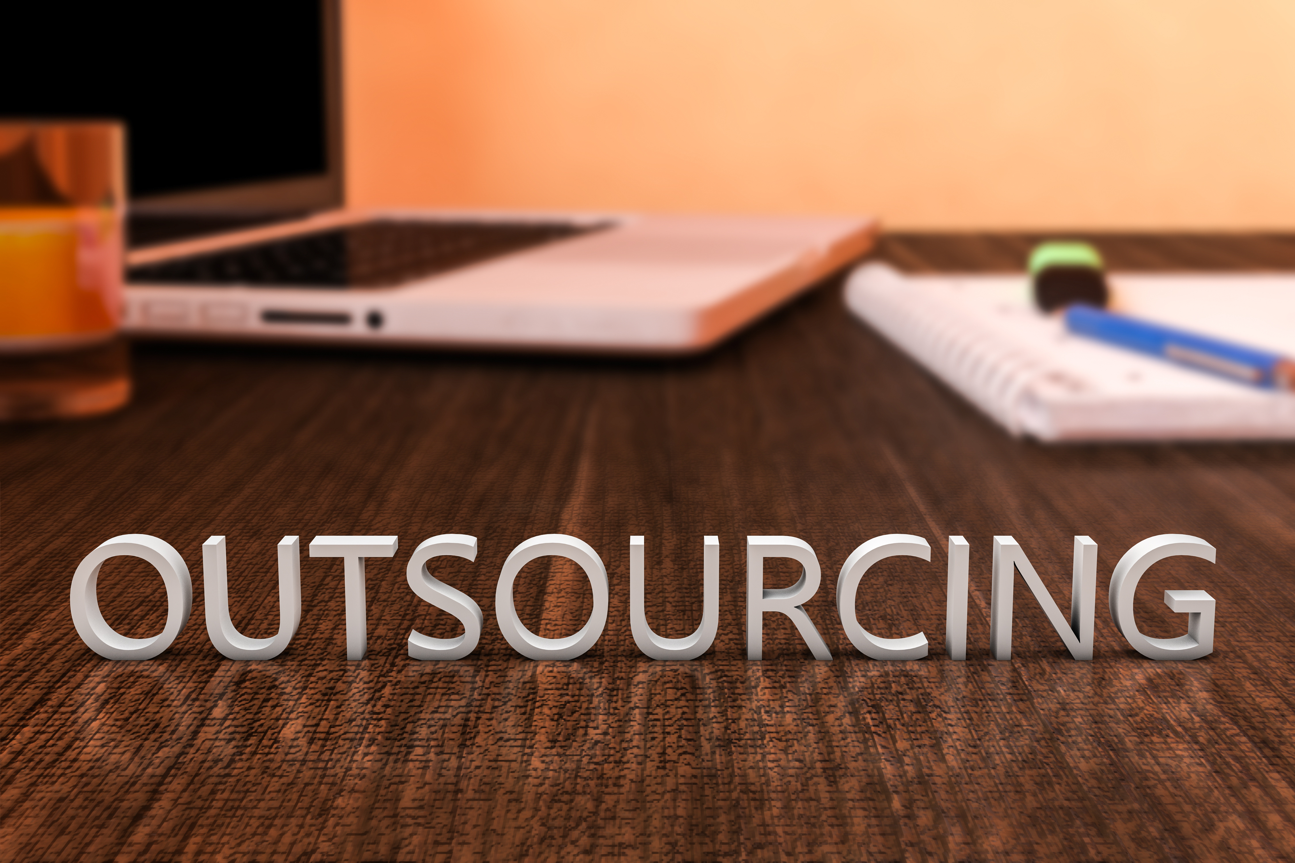Outsourcing - letters on wooden desk with laptop computer and a notebook. 3d render illustration.